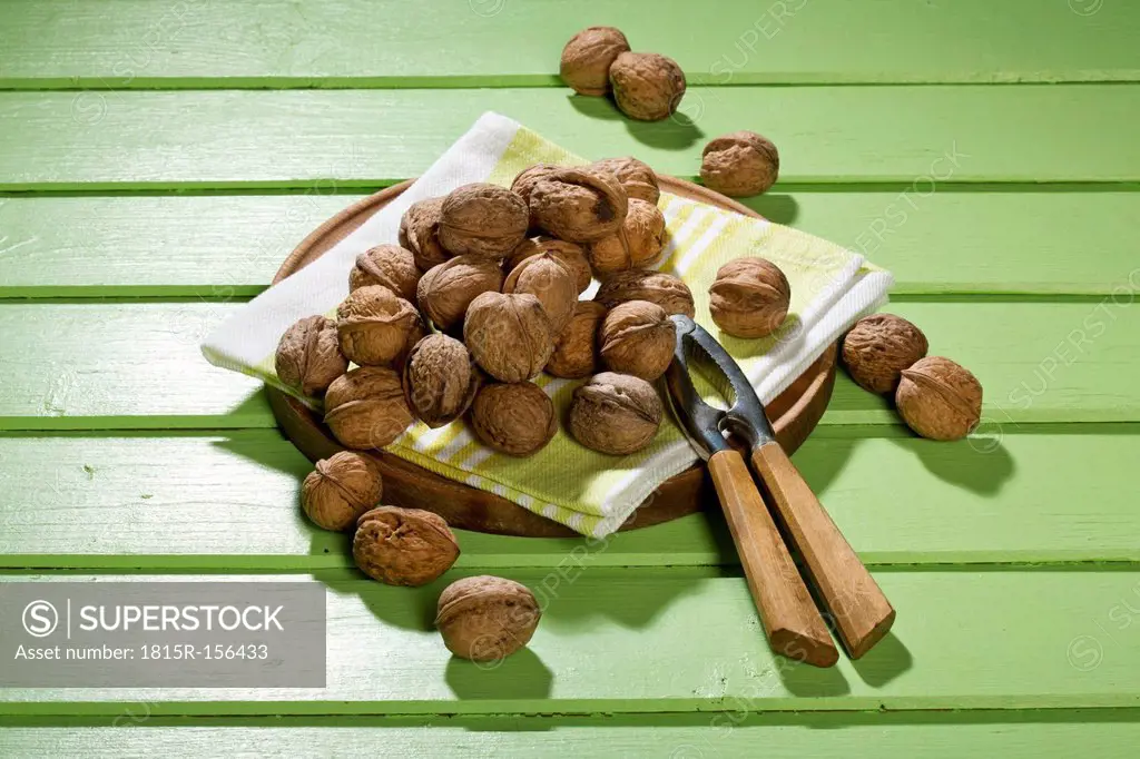 Walnuts (Juglans regia), nutcracker and napkin on green wooden table
