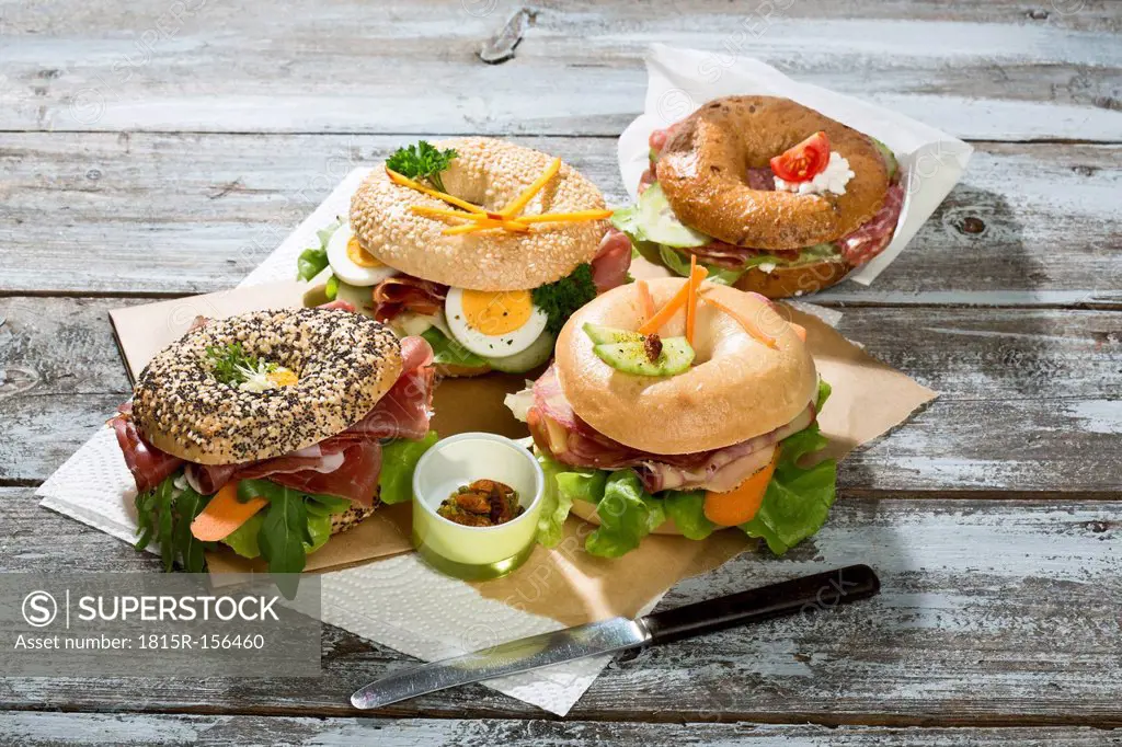 Four different bagels garnished with salami, sausage, slices of bacon, rocket salad, tomato, lettuce, cucumber carrot, egg, cream cheese and cress and...