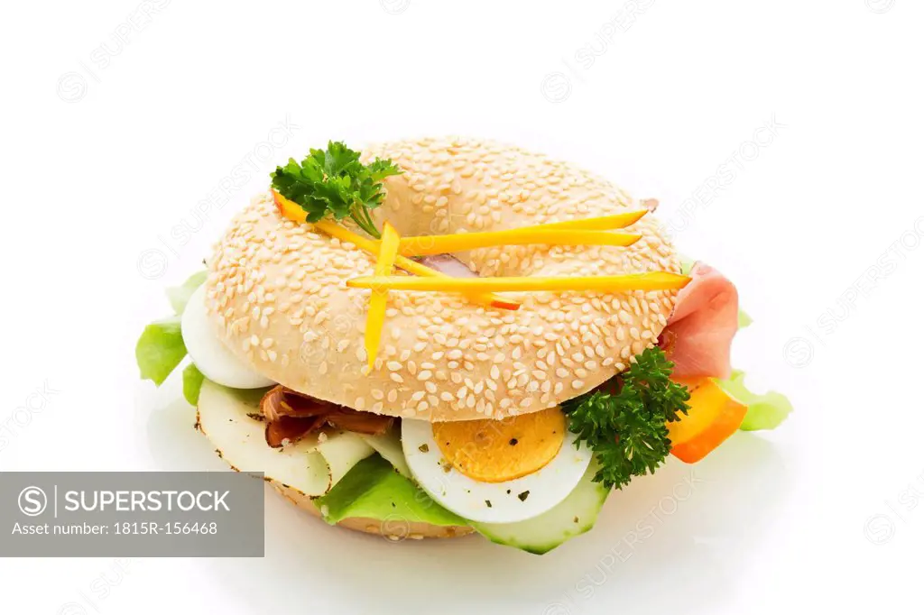 Sesame seed bagel garnished with slices of bacon, lettuce, cucumber, carrot, egg, Fol Epi and parsley