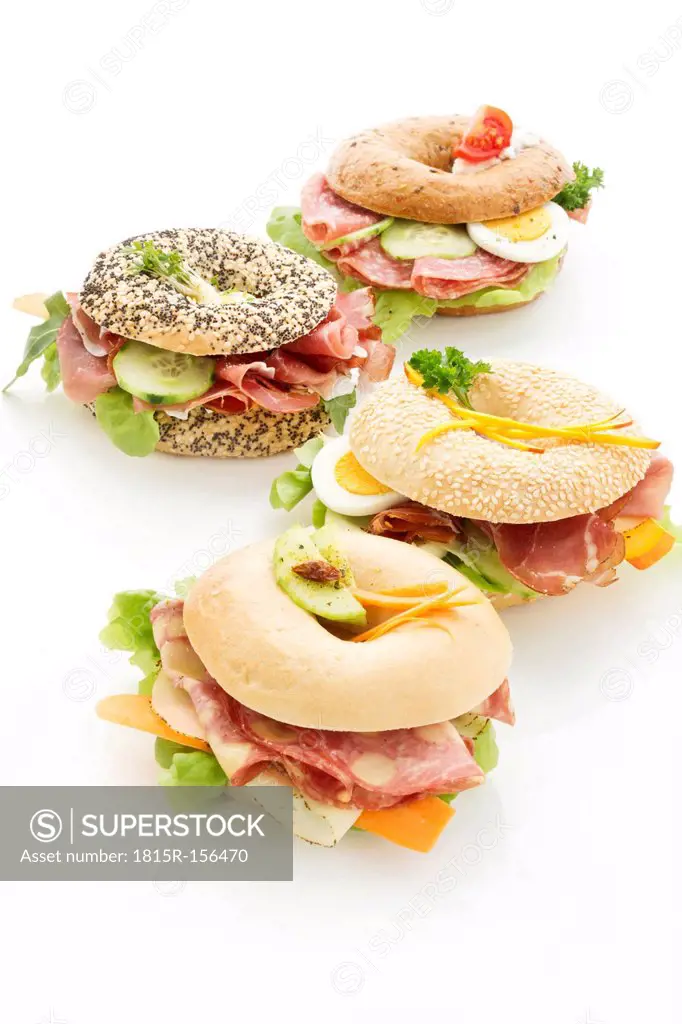 Four different bagels garnished with slices of bacon, lettuce, cucumber, carrot, tomato, Fol Epi, egg, cream cheese and cress and parsley