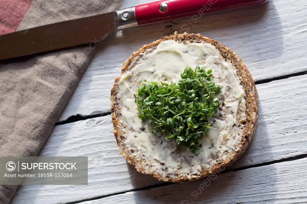 Slice of wholemeal bread with cress, heart-shaped and knife on wooden table