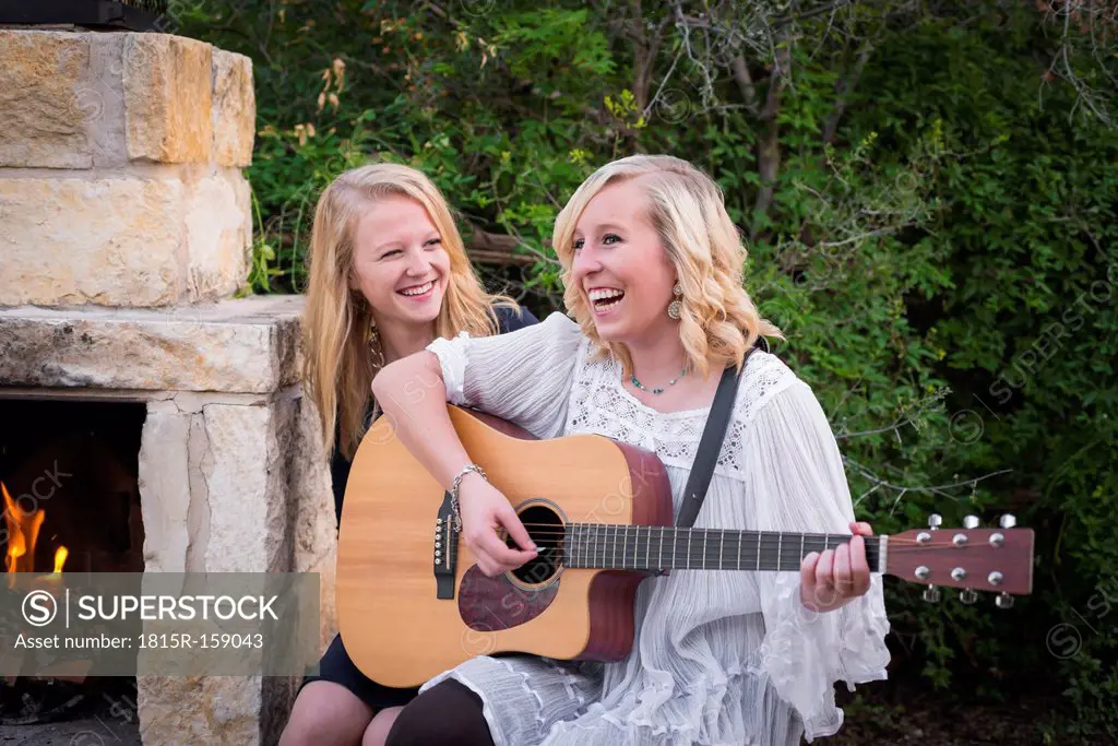 USA, Texas, Two happy teenage girls with guitar by the fireside