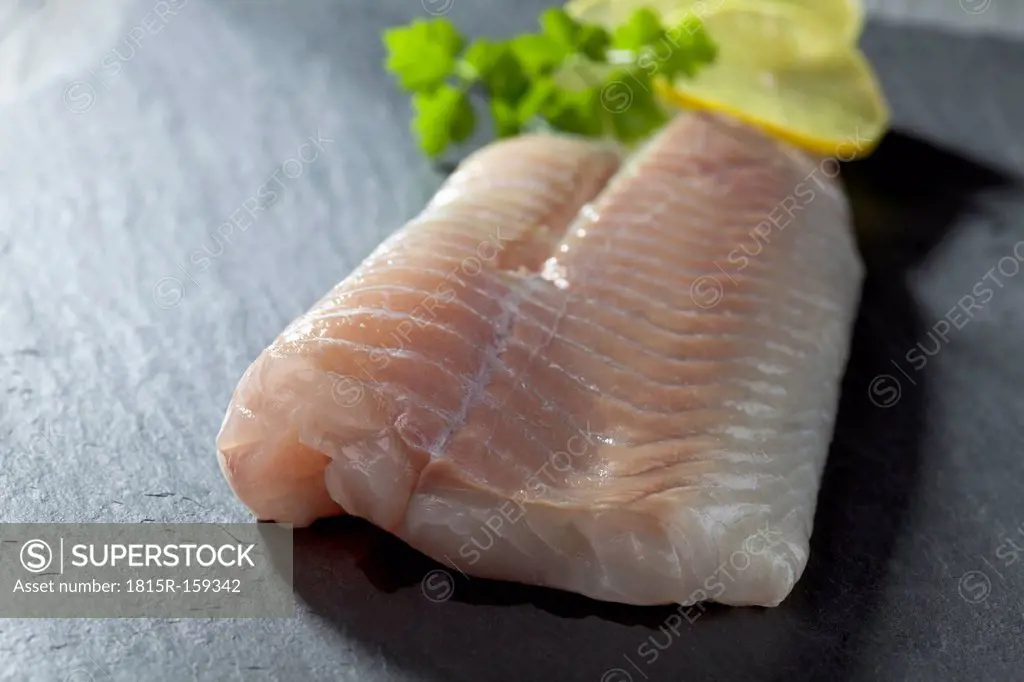 Fish fillet of coalfish with slices of lime on grey background