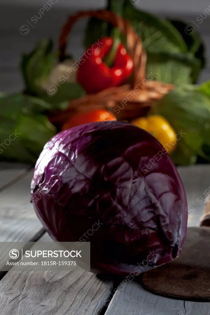 Red cabbage (Brassica oleracea convar. capitata var. rubra) and basket with other vegetables at background on grey wooden table