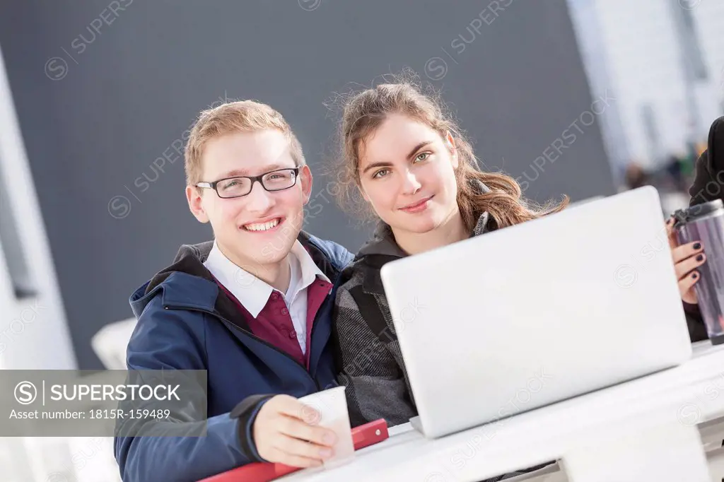 Two smiling students with laptop outdoors, portrait