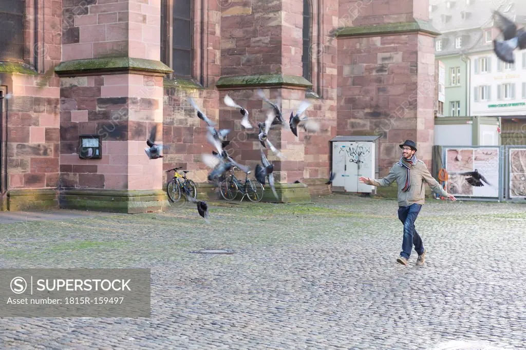 Germany, Baden-Wuerttemberg, Freiburg, Young man running behind pigeon