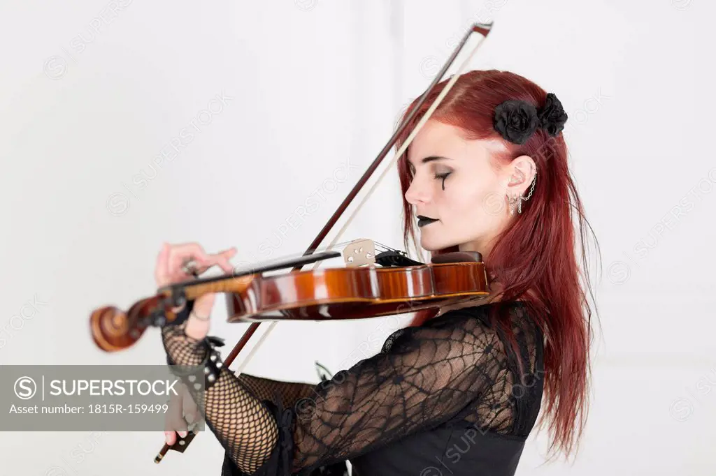 Young woman dressed in Gothic style playing violin with closed eyes