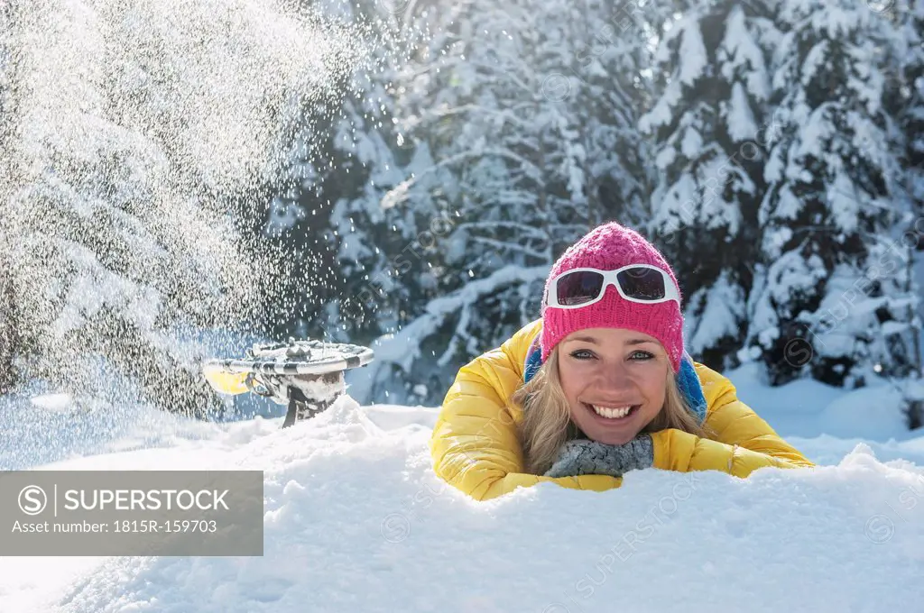 Austria, Salzburg State, Altenmarkt-Zauchensee, Smiling young woman lying in snow, portrait