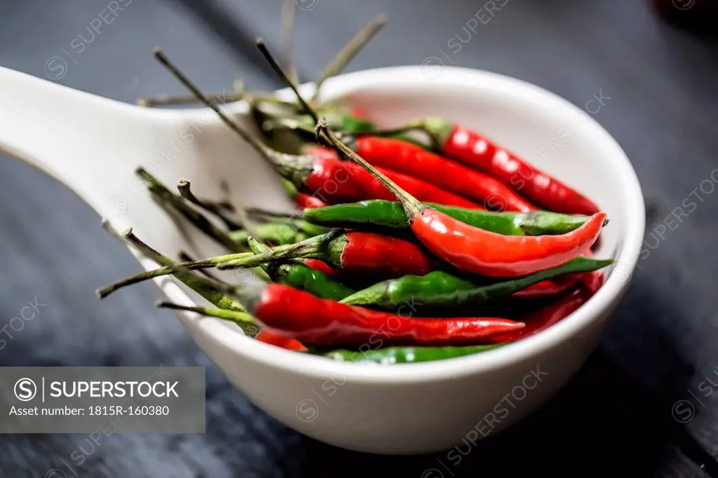 Red and green chilli peppers in a white bowl on wooden table