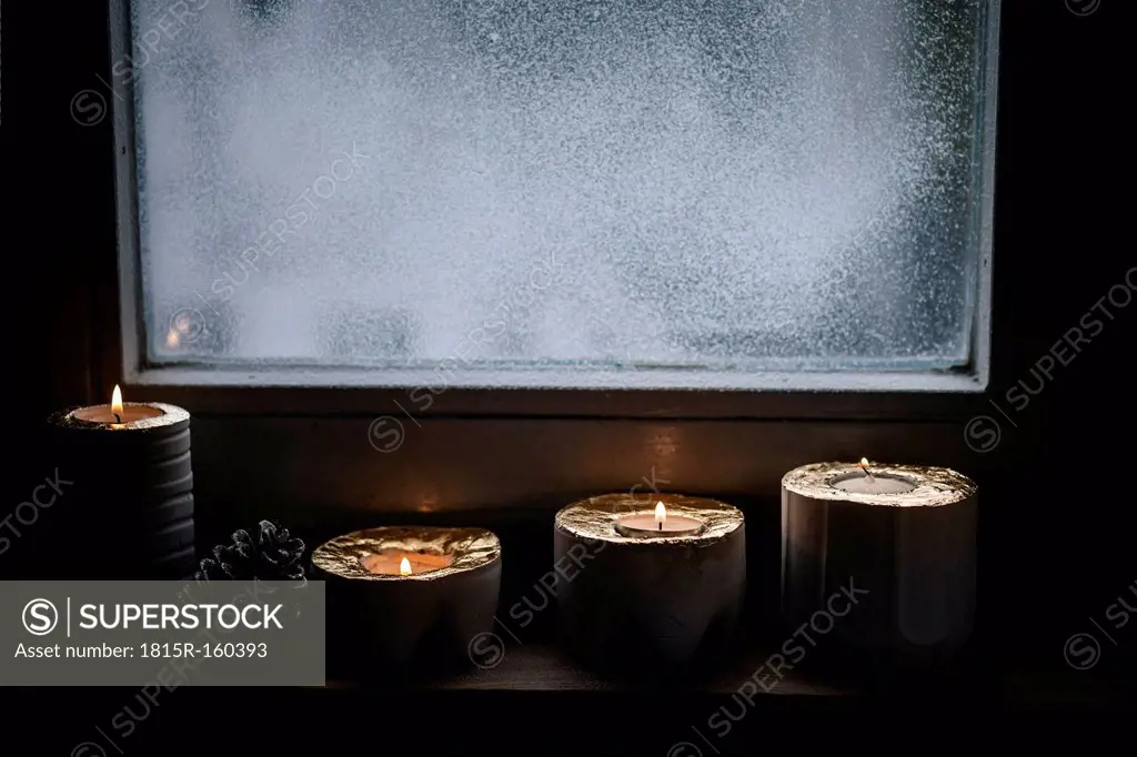 Four lighted advent candles and a fir cone in front of snow covered window