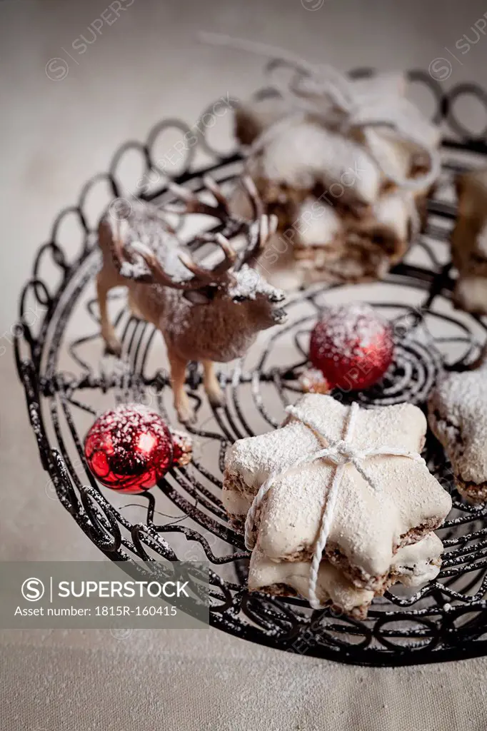 With powdered sugar sprinkled star-shaped cinnamon cookies, miniature deer and red Christmas baubles on cake stand