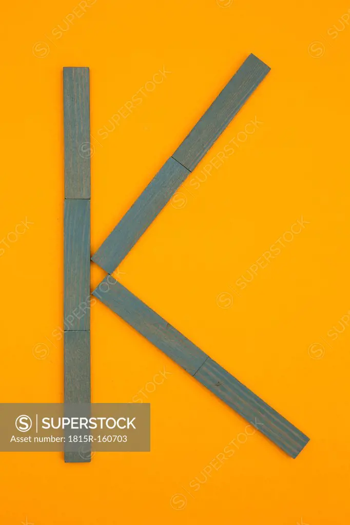 Letter K formed of blue building bricks at yellow background, studio shot