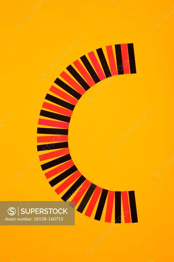 Letter C formed of red and black paper stripes at yellow background, studio shot