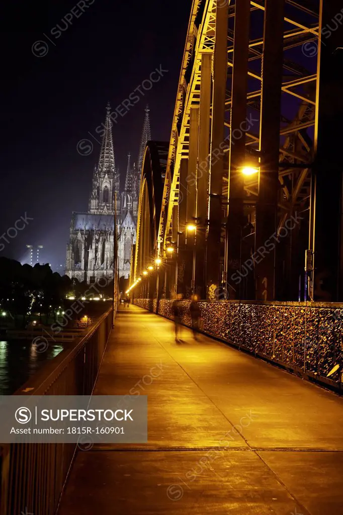 Germany, North Rhine-Westphalia, Cologne, lighted Cologne Cathedral and Hohenzollern Bridge with pedestrians at night