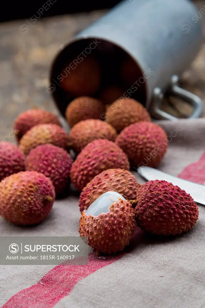 Litchis (Litchi chinensis), kitchen towel and metal cup on wooden table