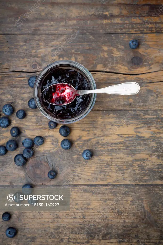 Blueberries (Vaccinium myrtillus) and glass of blueberry jam with spoon on wooden table