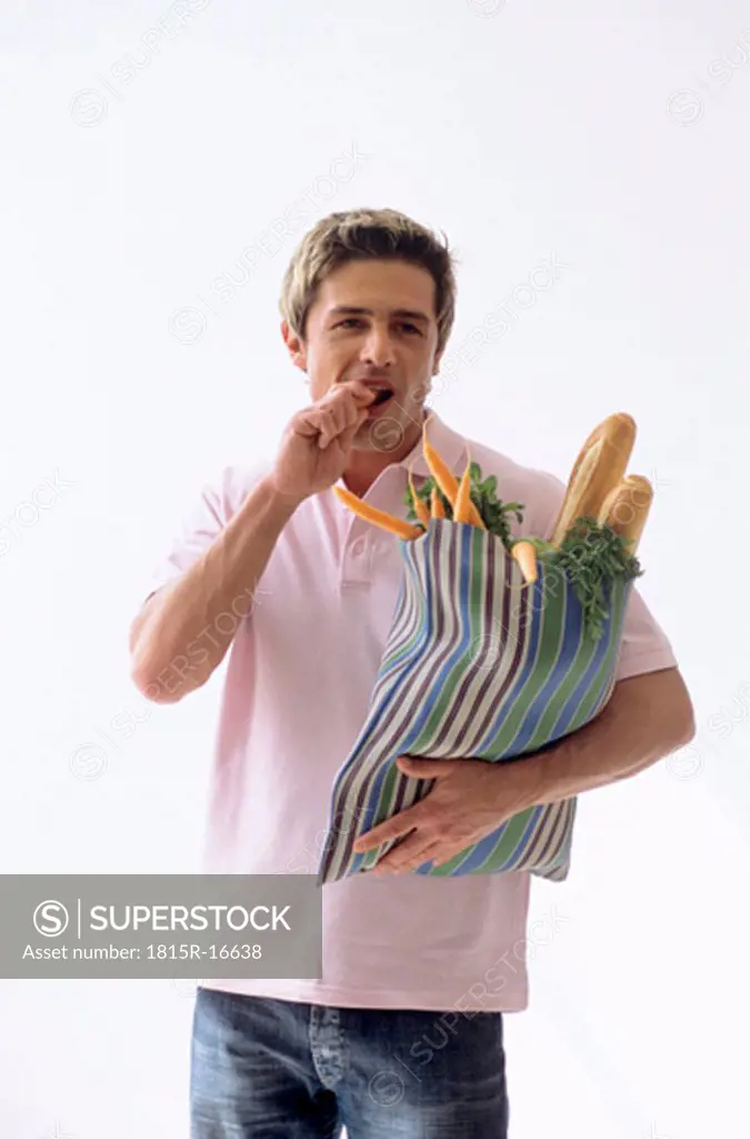 Man carrying grocery bag, eating carrot