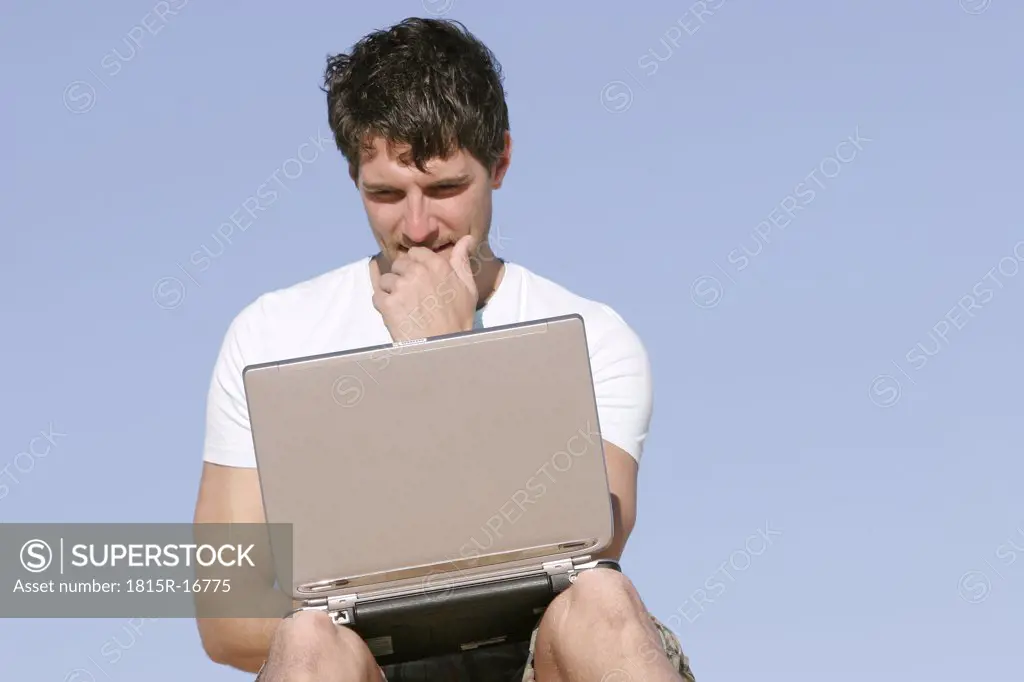 Man sitting outdoors with laptop on his knees