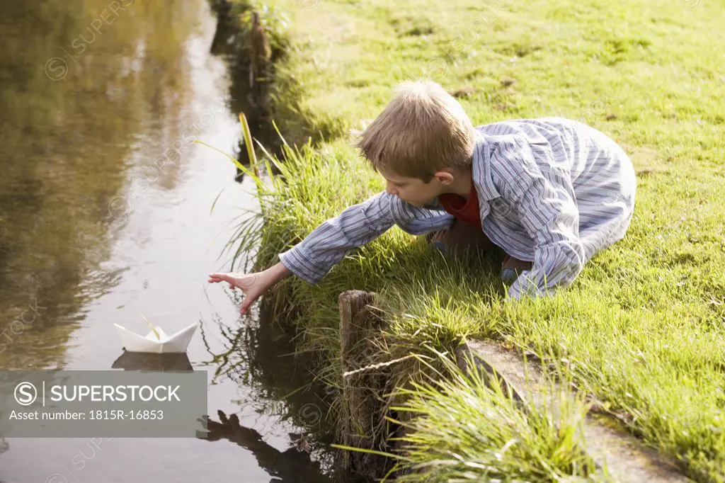 Boy (10-12) putting paper boat in river, side view