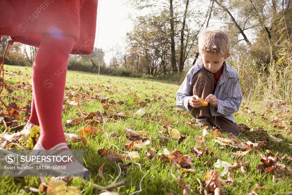 Boy (10-12) sitting in meadow,legs of girl in foreground