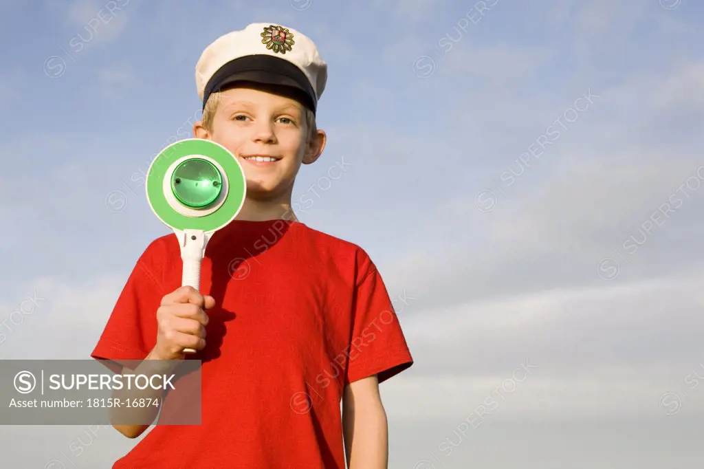 Boy (10-12) wearing police cap, holding green sign