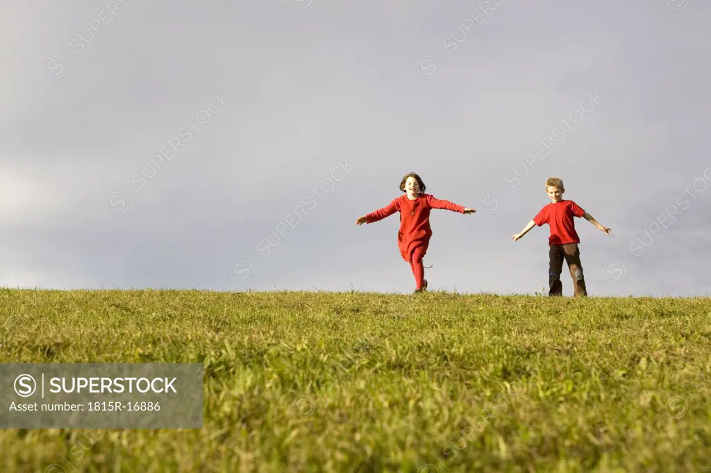 Boy (10-12) and girl (7-9) running in meadow, arms outstretched