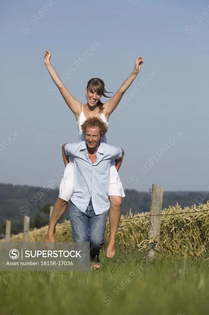 Germany, Bavaria, Man giving woman piggyback in meadow, laughing