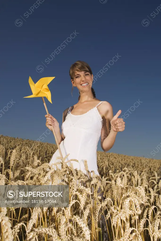 Germany, Bavaria, Young woman standing in field, holding pinwheel, portrait