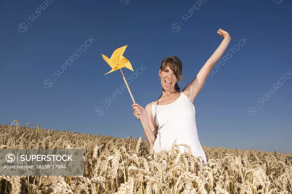 Germany, Bavaria, Young woman standing in field, holding pinwheel, portrait