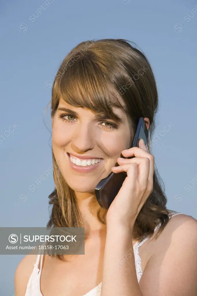 Germany, Bavaria, Young woman using mobile phone, smiling, portrait
