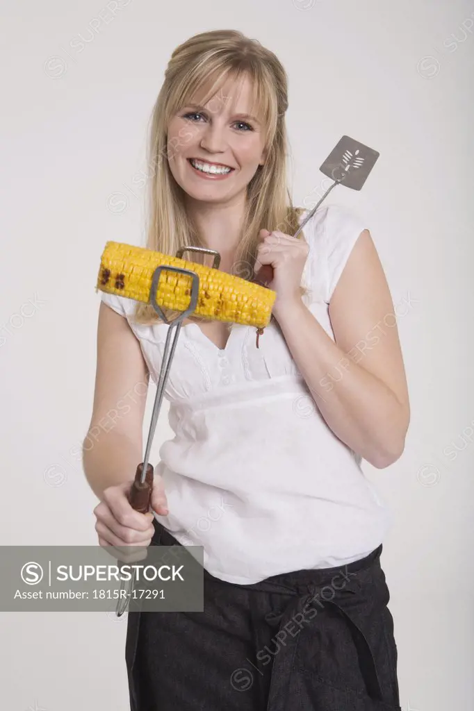 Young woman holding a maize cob with barbecue tongs