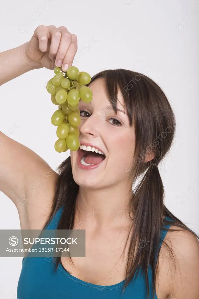 Yöung woman holding bunch of grapes, mouth open, portrait
