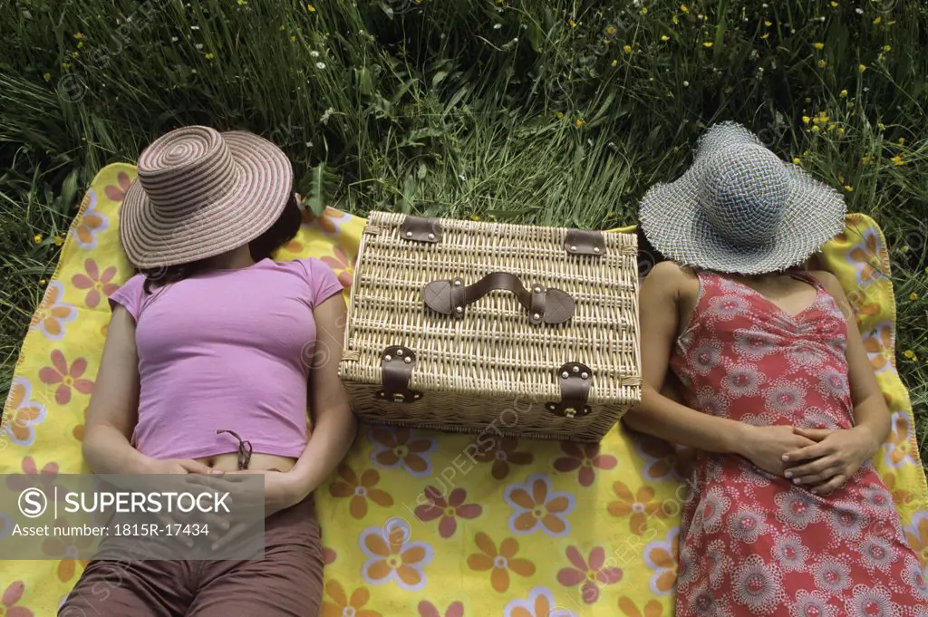 Women relaxing in meadow with hat over face