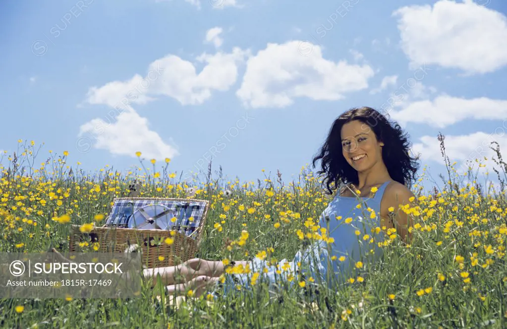 Young woman sitting in a flower meadow, having picnic