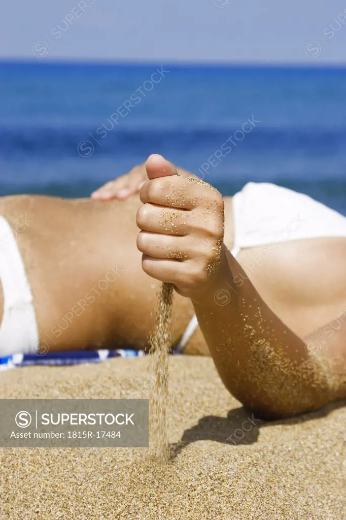 Woman in bikini lying on beach, mid-section