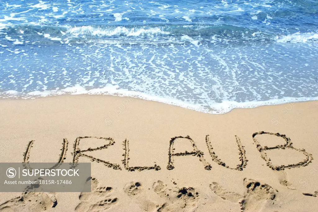 Word 'urlaub' (Vacation) written in sand on beach