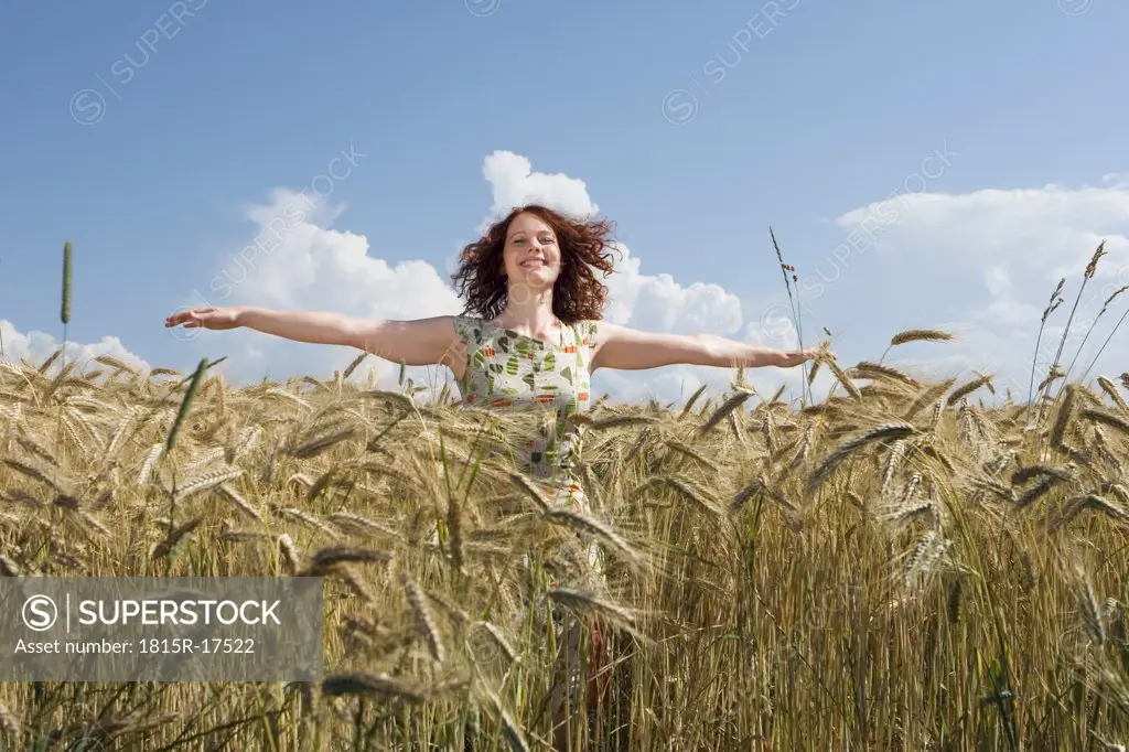 Young woman standing in cornfield, smiling, arms outstretched