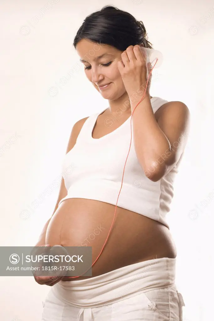 Pregnant woman, holding cup on belly and ear