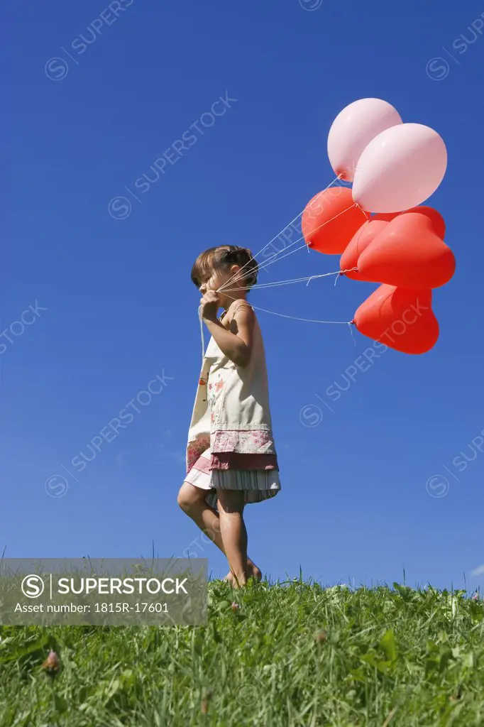 Girl (7-9) holding bunch of balloons, side view