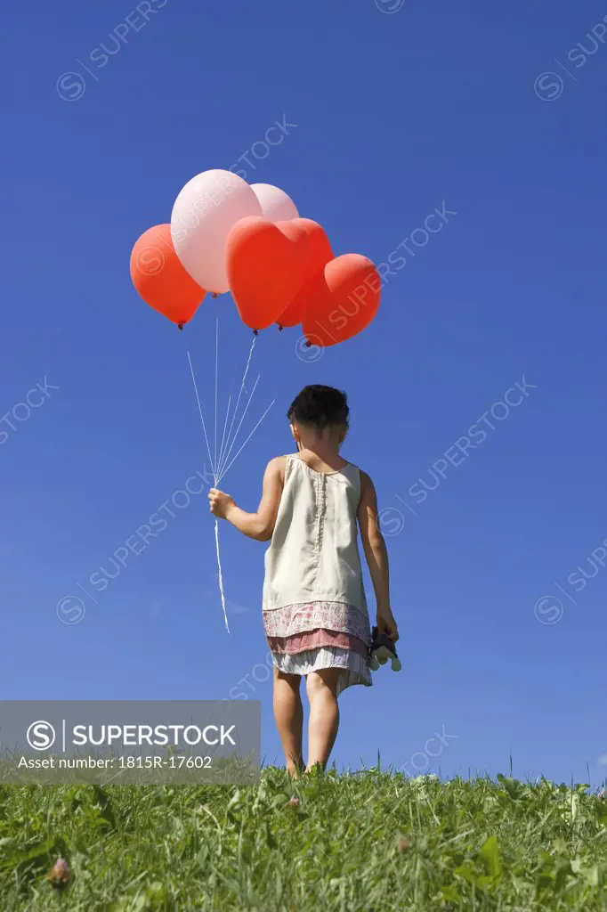 Girl (7-9) holding bunch of ballons, rear view