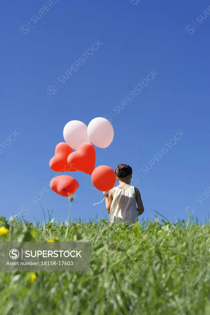 Girl (7-9) holding bunch of ballons, rear view