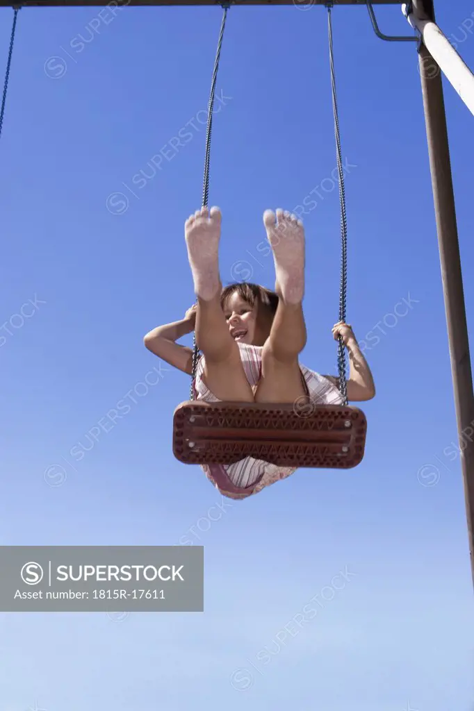 Girl (7-9) sitting on swing, feet up