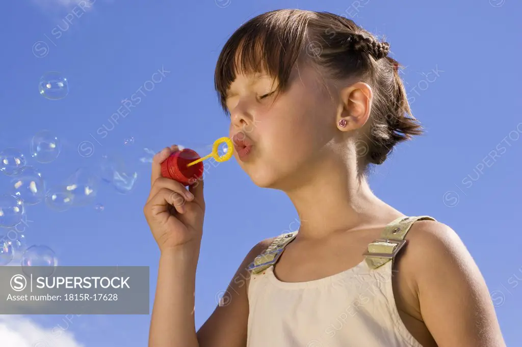 Girl (7-9) blowing soap bubbles, eyes closed, close-up