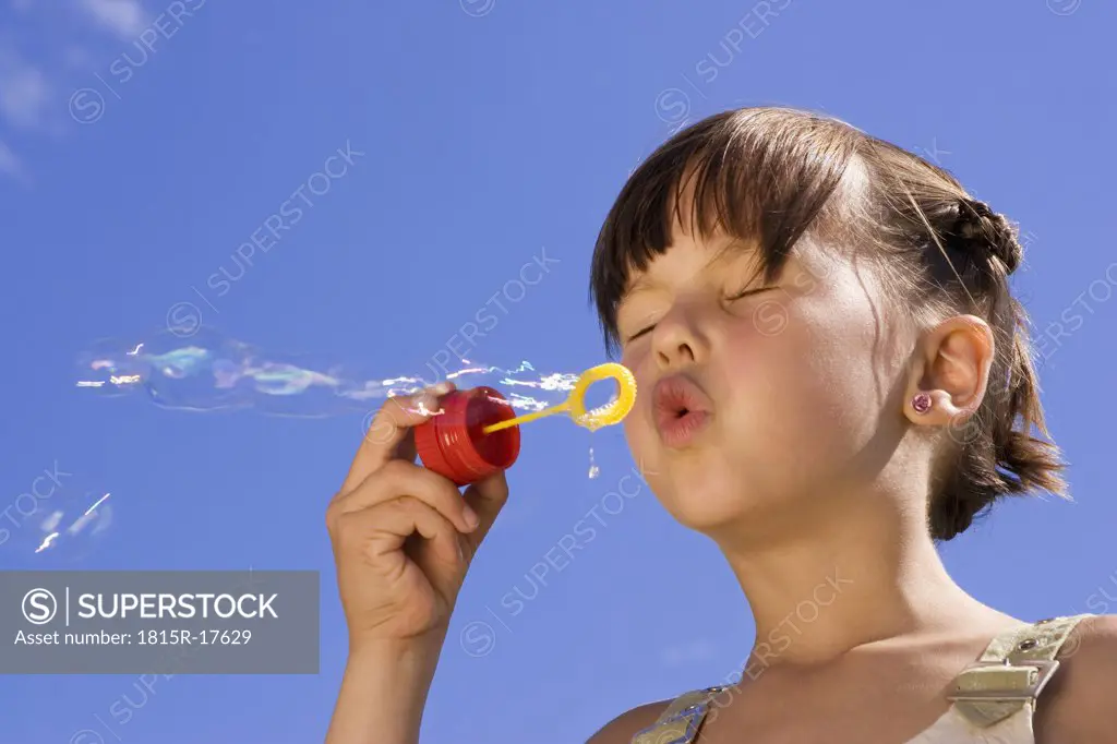 Girl (7-9) blowing soap bubbles, eyes closed