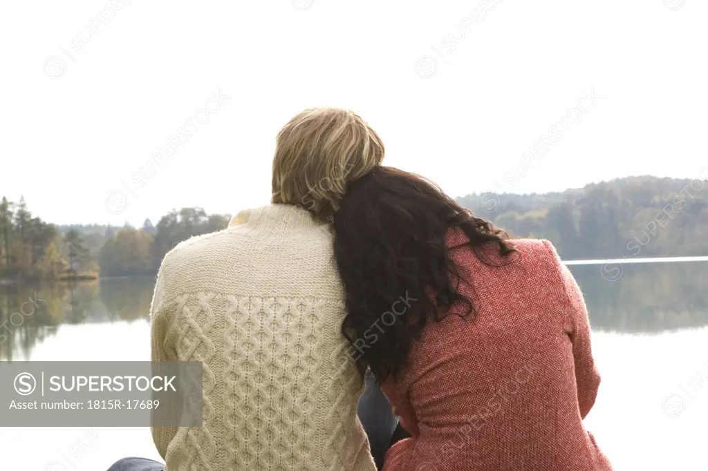 Young couple sitting at lake, rear view