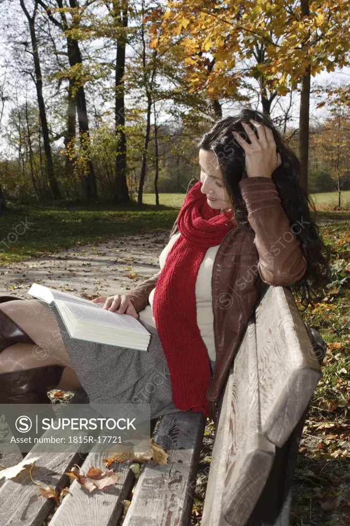 Young woman sitting on bench, reading book