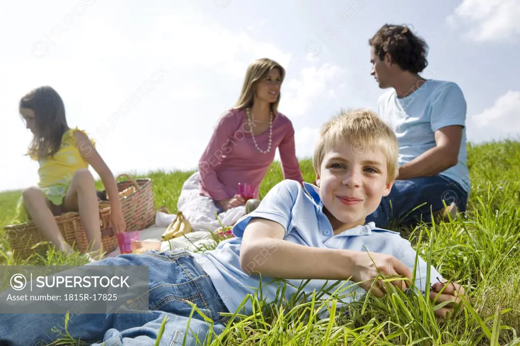 Boy lying in meadow, family in background