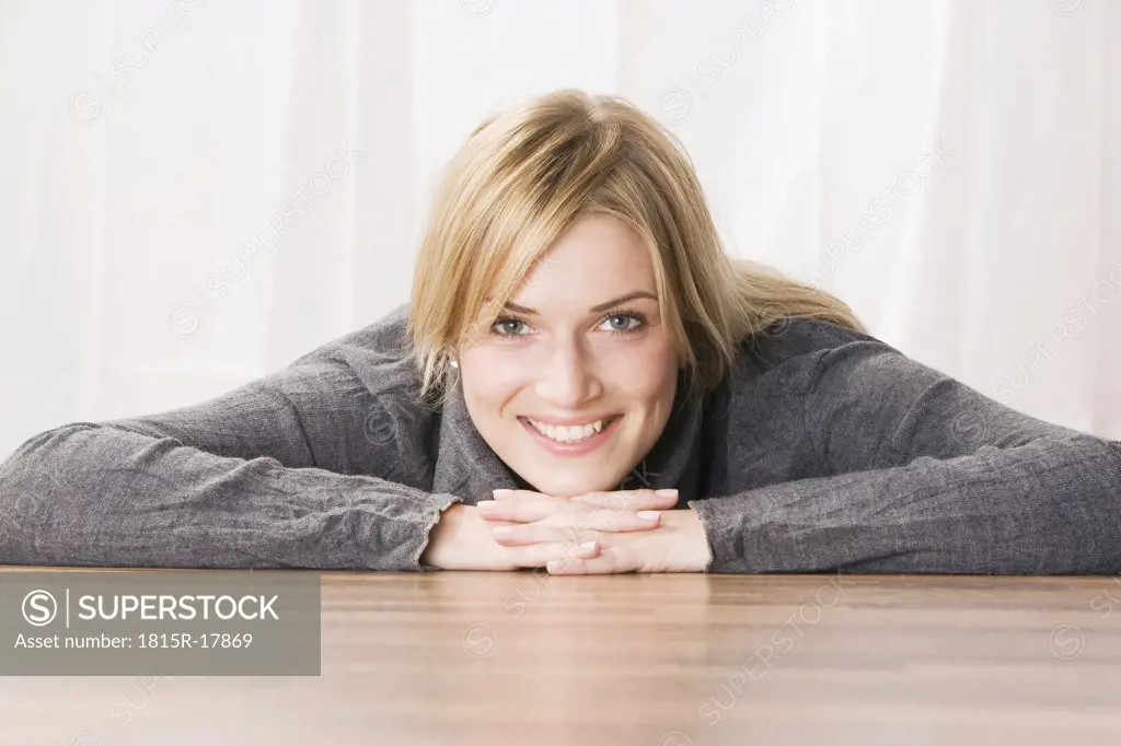 Blonde woman, head resting on hands, smiling, portrait