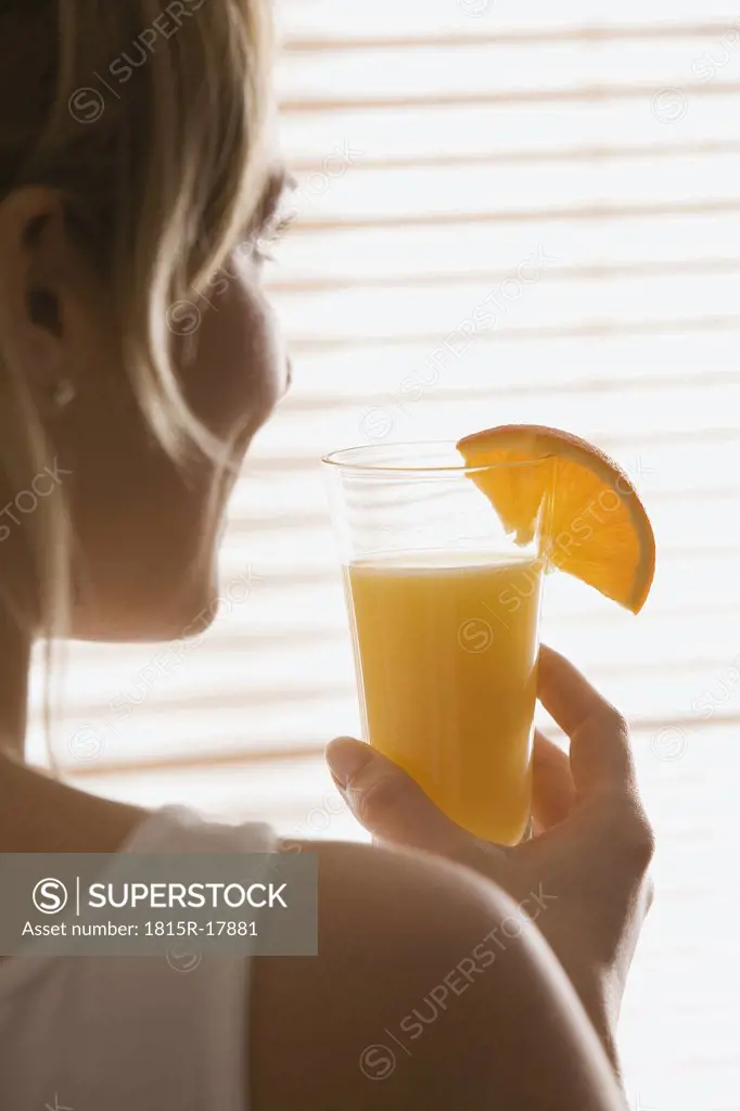 Blonde woman holding a glass of orange juice, rear view