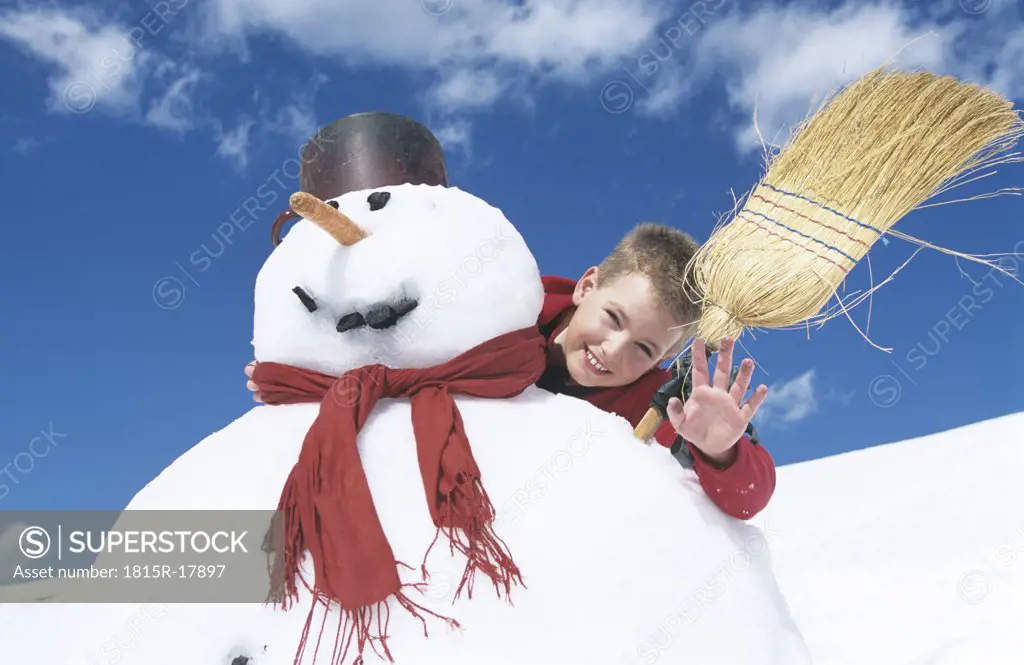 Boy standing behind snowman with broomstick